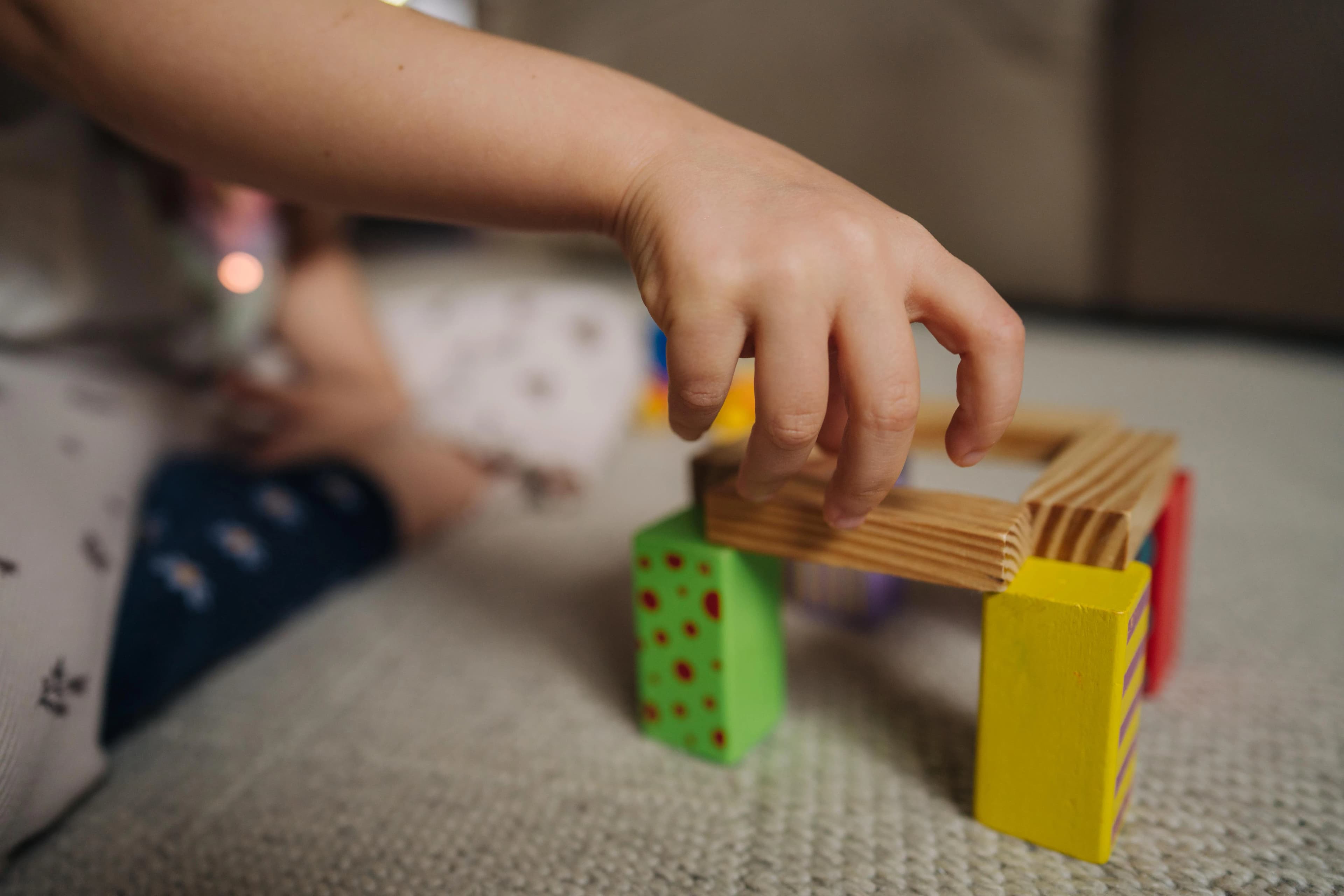 Child’s hands building a small structure using wooden blocks